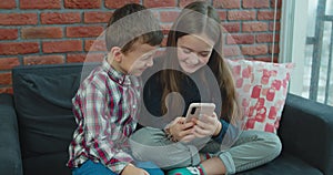 Portrait of kids looking at mobile phone at home. Sister and brother playing video games on mobile phone.