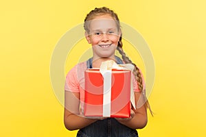 Portrait of kind merry little girl with braid holding gift box and smiling to camera, child enjoying birthday present