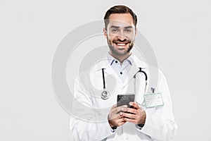 Portrait of kind young medical doctor with stethoscope working in clinic and holding cellphone