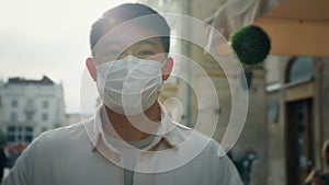 Portrait korean man wearing medical mask standing on street in sunlight looking at camera young asian male tourist in