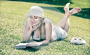 Portrait of l woman lying on green lawn in park and reading book