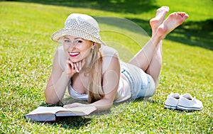 Portrait of l woman lying on green lawn in park and reading book