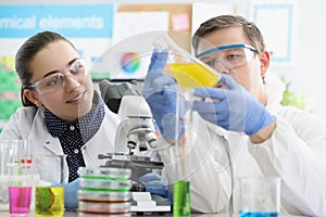 Laboratory workers man and woman examine yellow liquid in flask.
