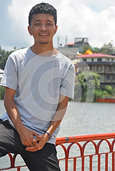 Portrait of a Ladakhi North Indian young guy sitting on safety barrier by lake and looking at camera