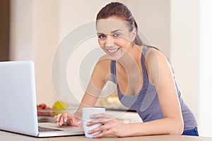 Portrait, laptop and coffee with a woman in the kitchen of her home to study or relax in the morning. Computer, smile