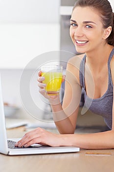 Portrait, laptop and smile for orange juice with a woman in the kitchen of her home to relax in the morning. Computer