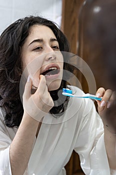 portrait of a latin woman holding a toothbrush looking at her molars and teeth in the mirror.