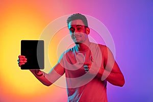 Portrait of Latina young man tablet, digital device isolated on gradient yellow purple background in neon light. Concept