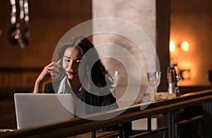 Portrait of laughing and beautiful businesswoman speaking on the phone and working on her laptop in modern restaurant