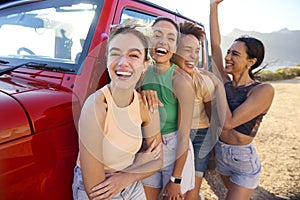 Portrait Of Laughing Female Friends On Vacation Having Fun Standing By Open Top Car On Road Trip