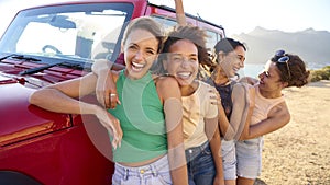 Portrait Of Laughing Female Friends On Vacation Having Fun Standing By Open Top Car On Road Trip