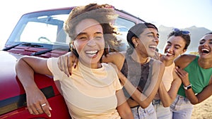 Portrait Of Laughing Female Friends On Vacation Having Fun Standing By Open Top Car On Road Trip