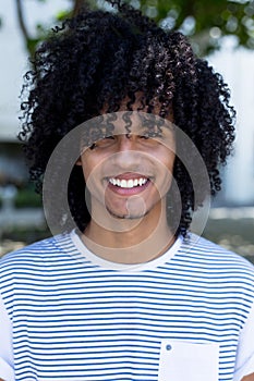 Portrait of laughing latin american young adult man with long curly hair
