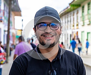 Portrait laughing Latino young man with cap and eyeglasses in a street of a town in Filandia Quindio