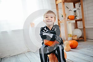 Portrait of laughing little boy in a skeleton costume is ready to celebrate Halloween. Boy in a halloween dress-up room.