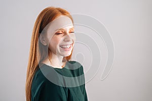 Portrait of laughing redhead young woman model holding hand near chin, closed eyes on white background.