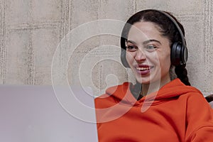 Portrait of a laughing woman 25-30 years old with headphones looking into a laptop.