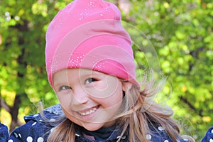 Portrait of laughing young girl child in pink cap and autumn clothes, blurred greenery bokeh background.