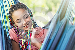 Portrait of laughing young girl with colorful braids in her hair posing on blue hammock