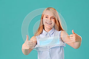 Portrait of a laughing young girl with a medical mask in her hands on a blue background. She is happy that the coronavirus has