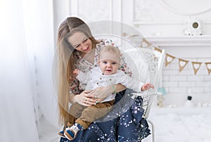 Portrait of laughing young mum together with a small son in a white room interior