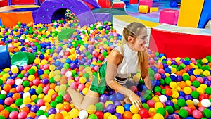 Portrait of laughing young woman falling in pool with lots of colorful plastic balls on the children palyground at photo