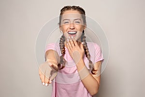 Portrait of laughing young woman pointing at viewer on light background