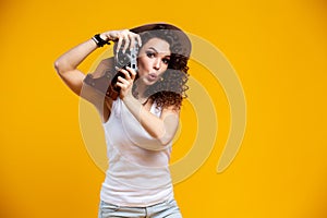 Portrait of laughing young woman taking pictures on retro vintage photo camera isolated on bright yellow background