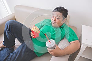 Lazy obese person eats junk food while laying on a couch