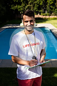 Portrait of lifeguard writing on clipboard at poolside