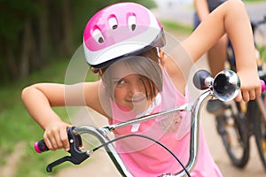 Portrait of a litte girl in a pink safety helmet driving her bike.