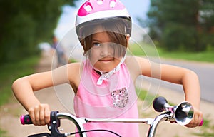 Portrait of a litte girl in a pink safety helmet driving her bike.