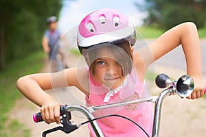 Portrait of a litte girl in a pink safety helmet driving her bike.