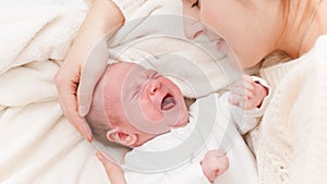 Portrait of little 1 months old baby boy crying on bed next to young mother