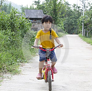 Portrait of little adorable Asian girl riding a bicycle on a countryside road. Family, holiday and healthy child concept