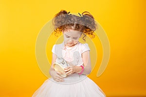 Portrait of a little adorable curly girl, looking frowned on a alarm clock, over yellow background. copy space.