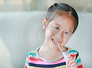 Portrait of little Asian child girl feeding liquid medicine with a syringe by self