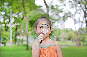 Portrait little Asian child girl looking through magnifying glass on park garden