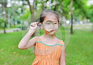Portrait little Asian child girl looking through magnifying glass on park garden