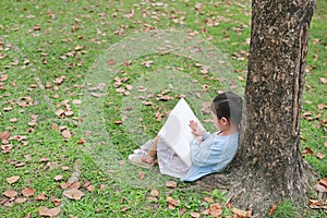 Portrait little Asian child girl reading book in park outdoor sitting lean against tree trunk in the garden outdoor