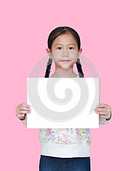 Portrait little asian child girl showing blank white paper isolated on pink background. Kid holding empty white square copy space