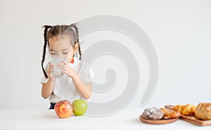 Portrait of little Asian girl drink milk and stand in front of apple and bread on white background