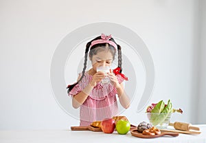 Portrait of little Asian girl drink milk and stand in front of vegetables and fruits on white background