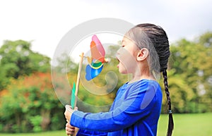 Portrait of little Asian kid girl blowing wind turbine in the summer garden