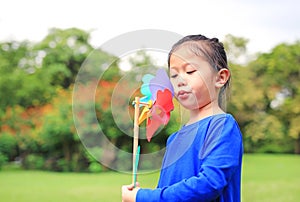 Portrait of little Asian kid girl blowing wind turbine in the summer garden