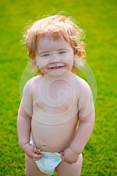 Portrait of a little baby boy in diaper playing outdoor in the grass. Baby and summer sunny weather. Funny little child