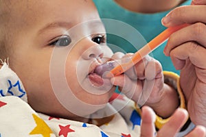 Portrait of little baby boy eating food. Baby with a spoon in feeding chair. Cute baby eating first meal