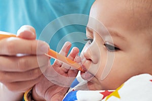 Portrait of little baby boy eating food. Baby with a spoon in feeding chair. Cute baby eating first meal