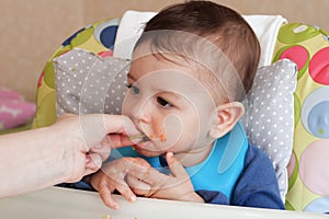 Portrait of little baby boy eating food. Baby with a spoon in feeding chair. Cute baby eating first meal