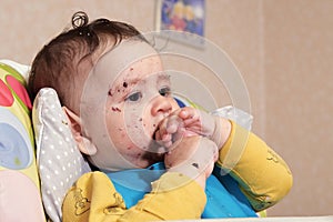 Portrait of little baby boy eating food. Baby with a spoon in feeding chair. Cute baby eating first meal